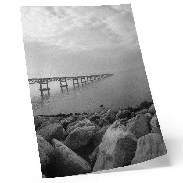 Poster paesaggio tranquillo con ponte e spiaggia rocciosa sotto un cielo grigio
