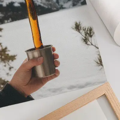 Foto su tela con stampa di una tazza che tiene una sostanza ambrata davanti a montagne innevate