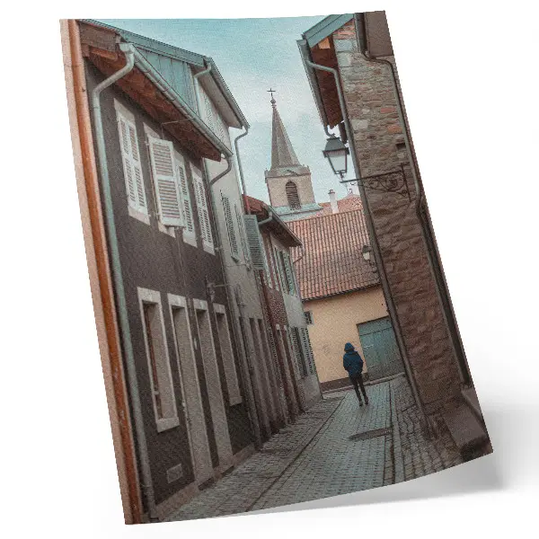 Poster via stretta con case popolari, torre e personaggio con cappotto blu